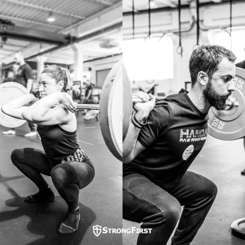 A woman does a barbell front squat while a man does a barbell back squat.