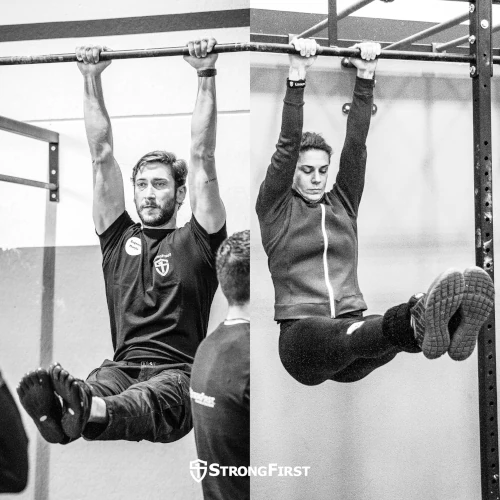 A woman and man both doing a strict hanging leg raise.